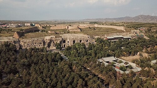 ​中国山西云冈石窟，北魏时期皇家佛教造像集中地。崖壁后上方为明代要塞，云岗堡遗址。东侧远山为丁崖山的风力发电场。